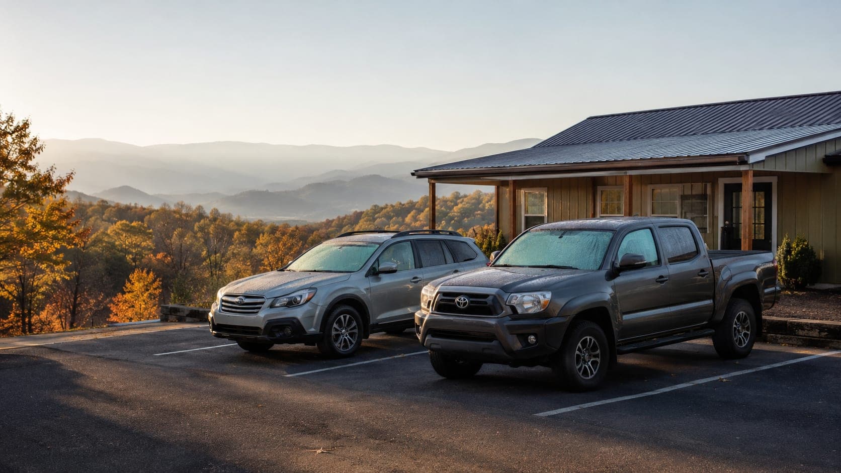 A silver Subaru Outback and a gray Toyota Tacoma parked outside a small office, with the Blue Ridge Mountains in autumn behind them
